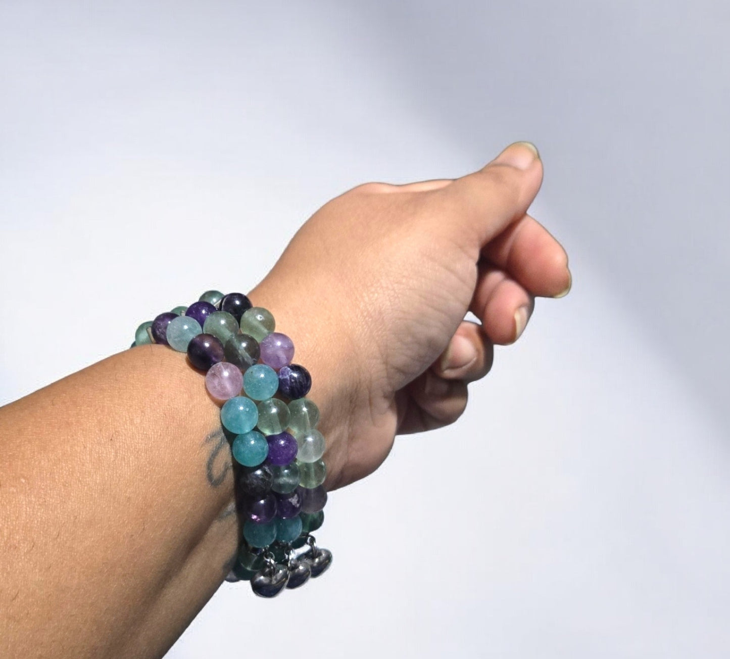 Handmade fluorite crystal stretch bracelet with green and purple beads and a silver heart charm displayed in natural light
