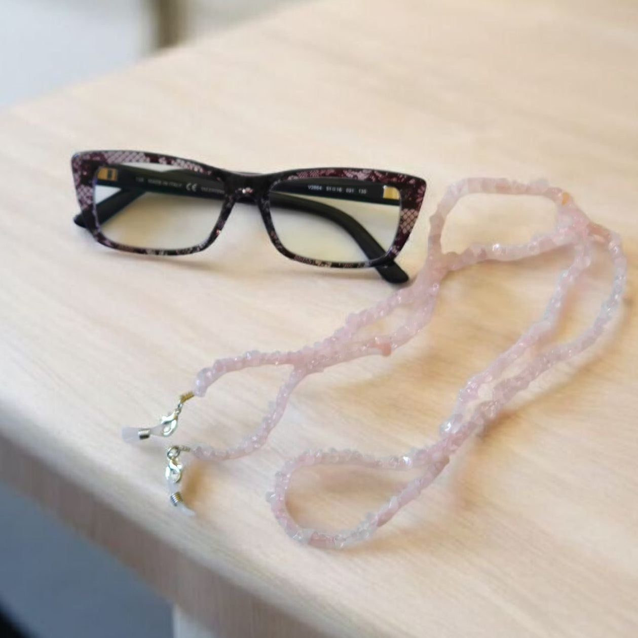 Eyeglasses with a Rose Quartz beaded lanyard on a wooden surface.
