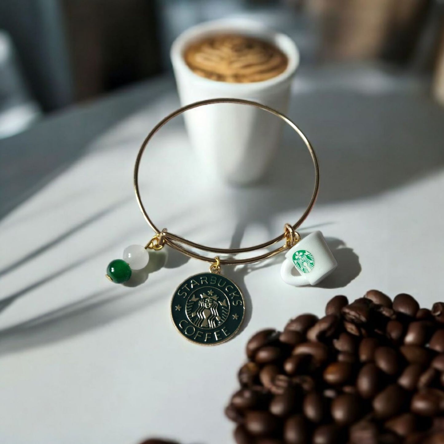 Gold toned Stainless Steel bracelet with green and white beads, a Starbucks coffee cup and logo charm on a surface with coffee beans and a cup in the background. Photo and Bracelet by Divalicious Designs.
