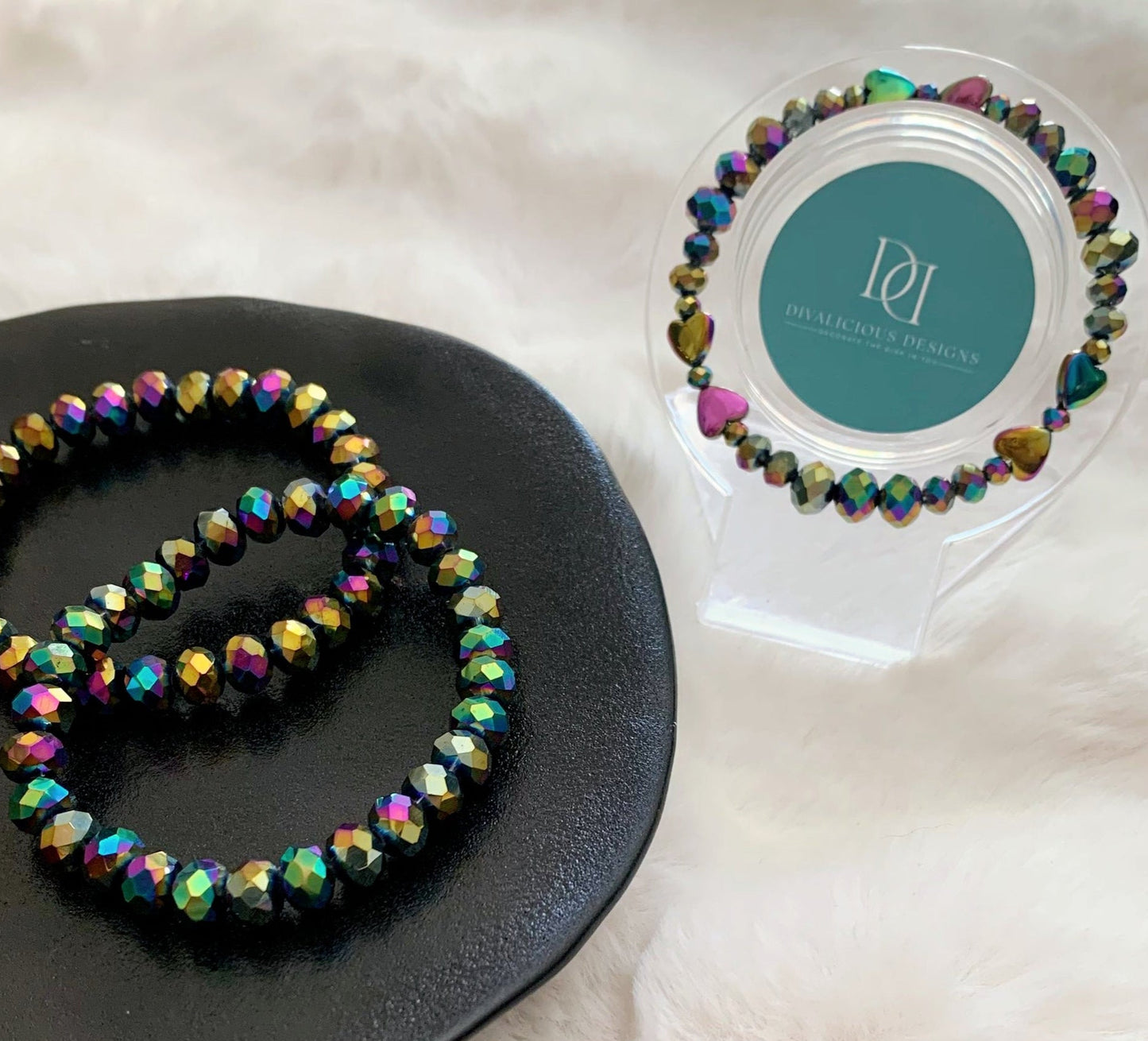 Multicolored beaded bracelet on a black plate with a branded display stand in the background. Made by Divalicious Designs.
