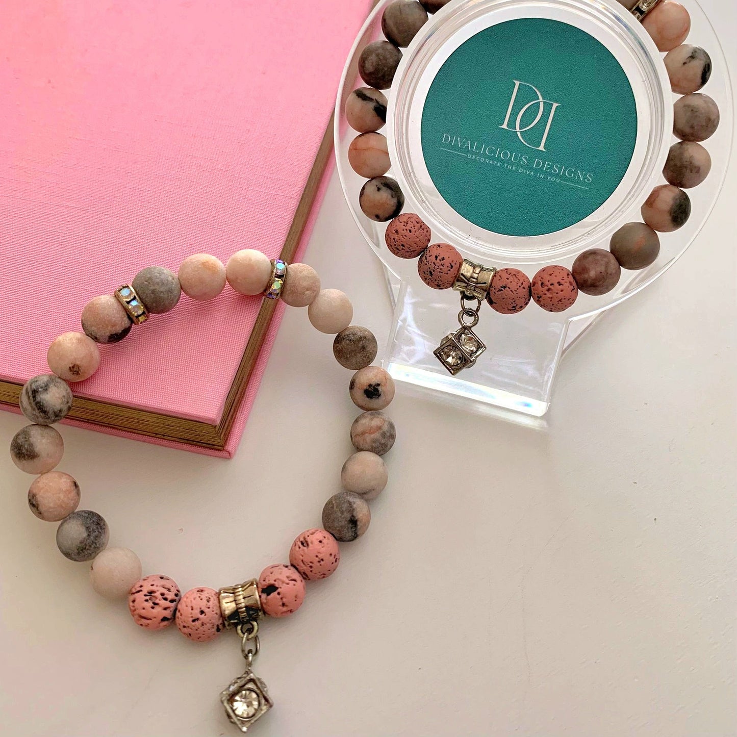 Pink Zebra Jasper bracelet with rhinestone spacers and a silver cubic zirconia cube charm displayed on pastel pink fabric.