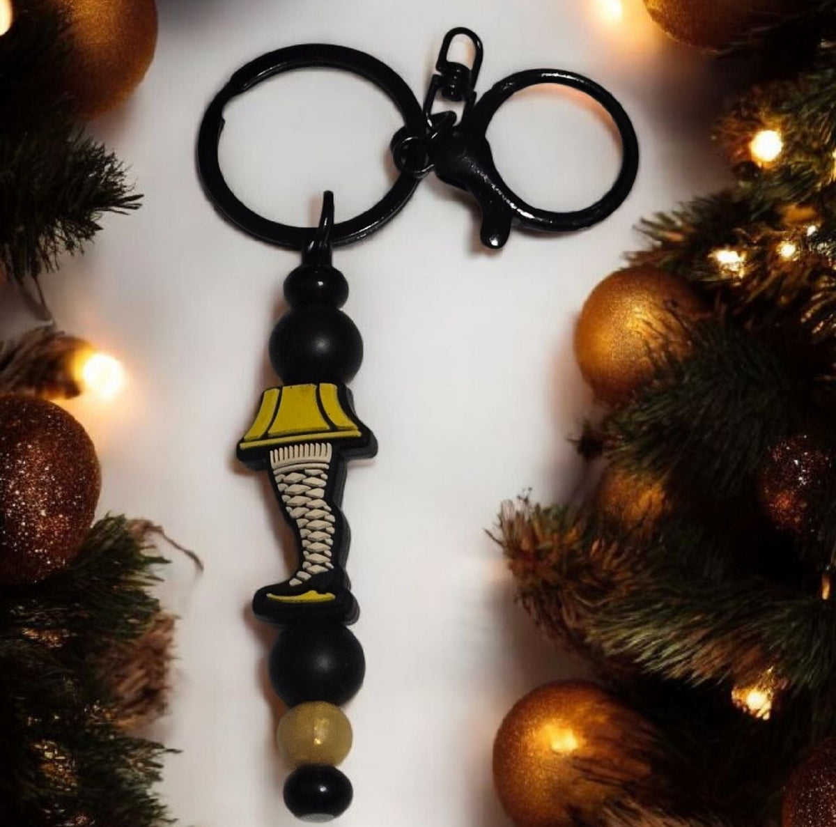 Decorative keychain with leg lamp from the movie, A Christmas Story on a white background surrounded by Christmas decorations. 