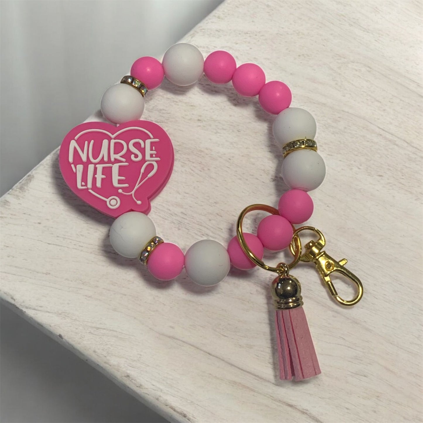 Pink and white beaded keychain with 'Nurse Life' tag on a light wooden surface