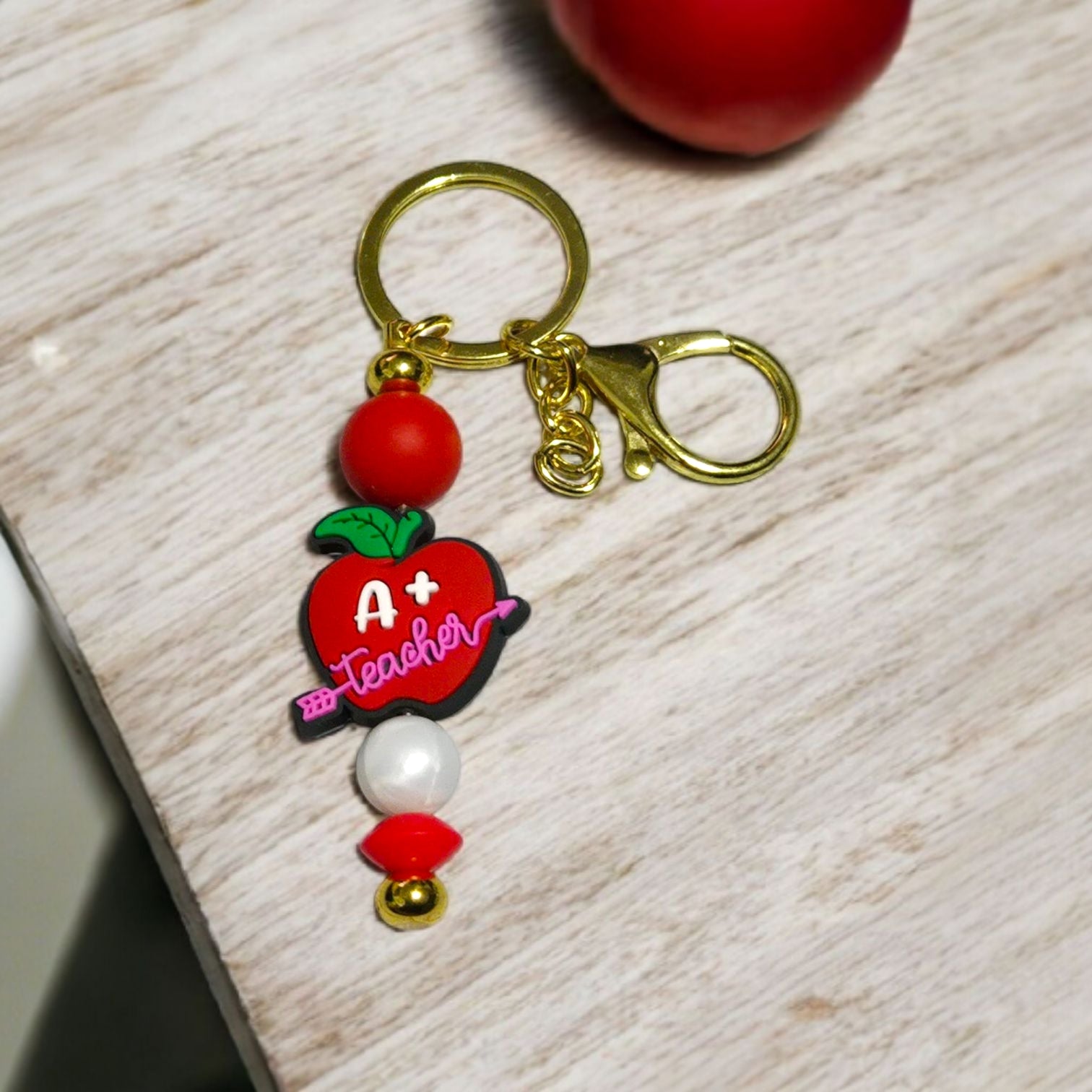 Keychain with red apple design and 'A+ Teacher' text on a wooden surface