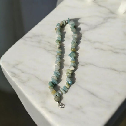 A phone lanyard made of Amazonite stone chip beads displayed on a light marble surface.  Photo and lanyard made by Divalicious Designs.