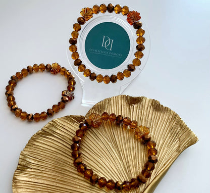 Two amber beaded bracelets on a gold leaf tray with a clear holder featuring a logo. Made by Divalicious Designs.