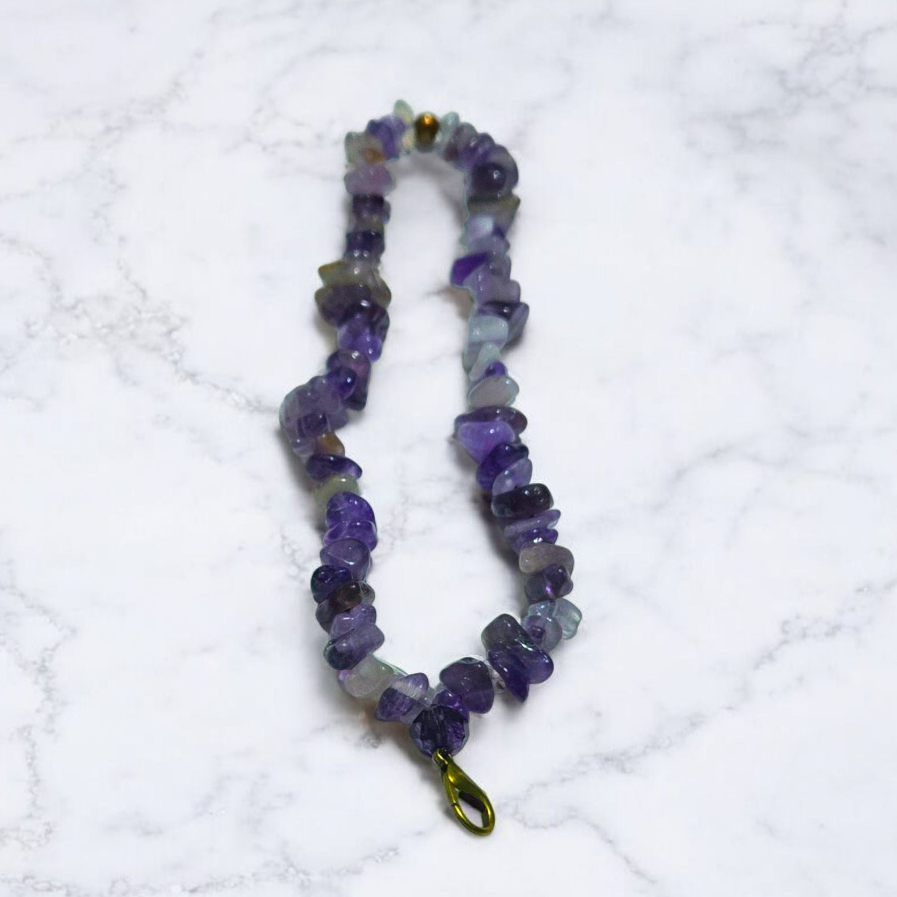 A phone lanyard made of Amethyst stone chip beads displayed on a light marble surface.  Photo and lanyard made by Divalicious Designs.