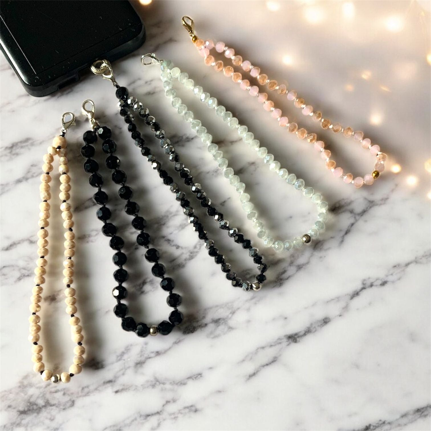Beaded crystal phone lanyards in assorted colours displayed on a marble surface; durable braided wrist straps designed for phone drop prevention.