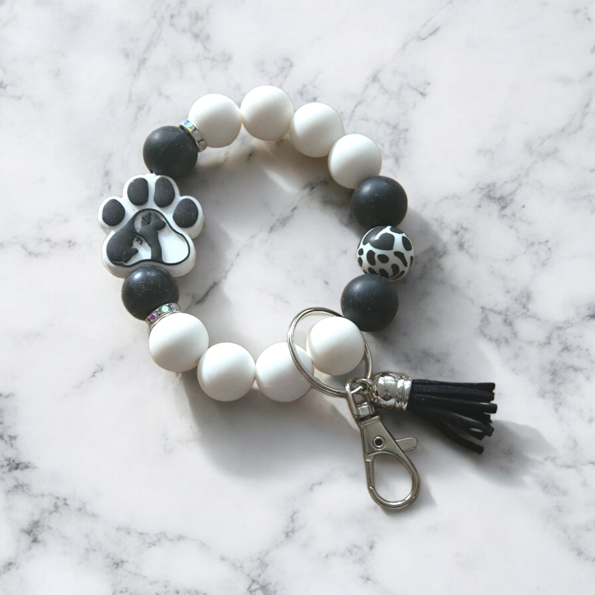 Pet themed silicone beaded wristlet with white and black beads and a tassel on a marble surface
