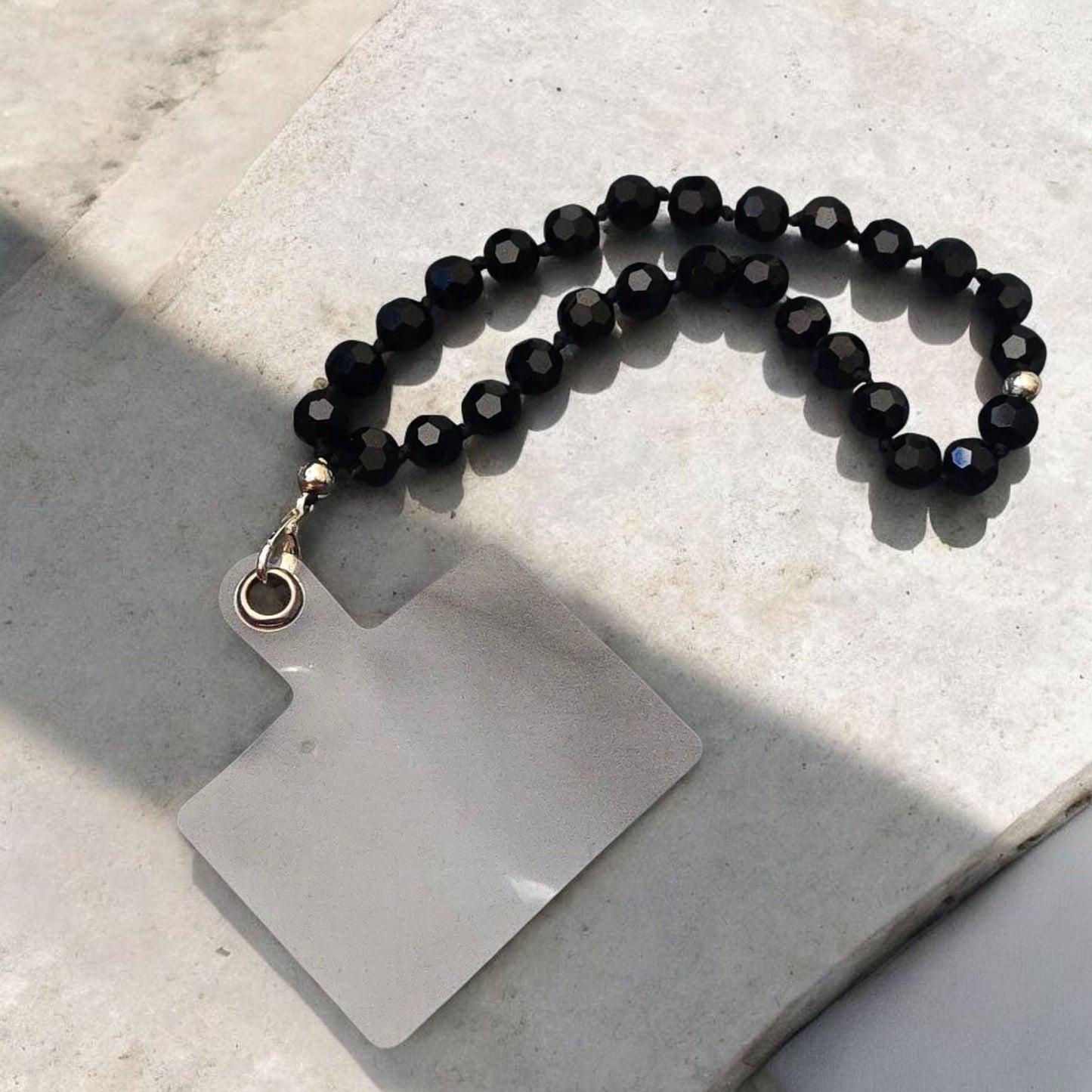Black Beaded Phone Lanyard Strap  displayed on a light stone surface.