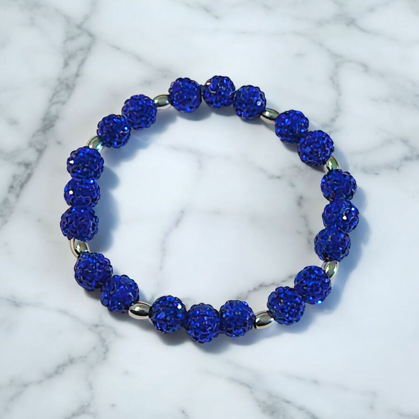 A Bracelet made of Royal Blue Shamballa beads and stainless steel beads laying on a marble surface. Picture and bracelet by Divalicious Designs.