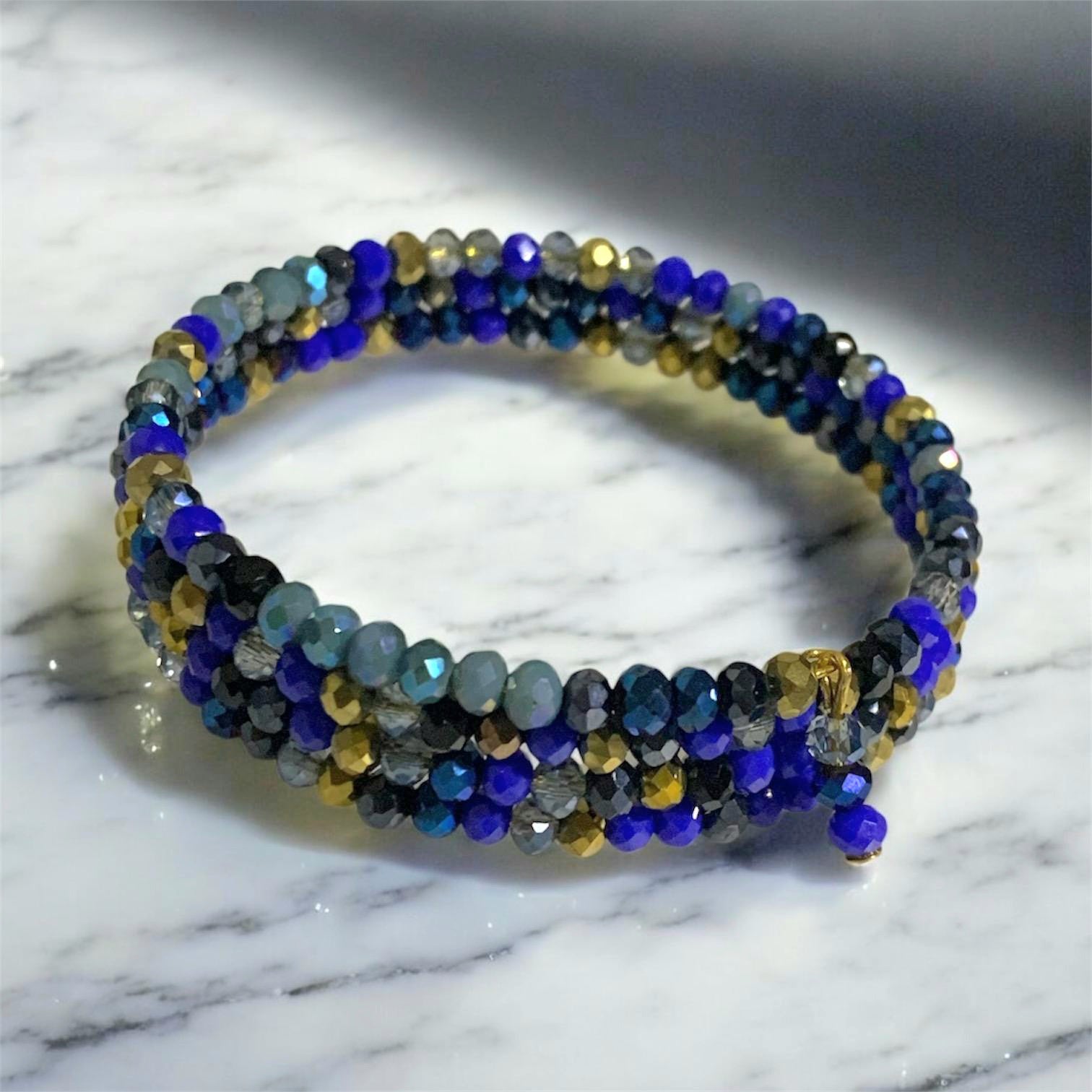 Austrian crystal memory wire wrap bracelet made with shimmering blue and crystals on carbon steel wire, featuring bead clusters and a small charm.
