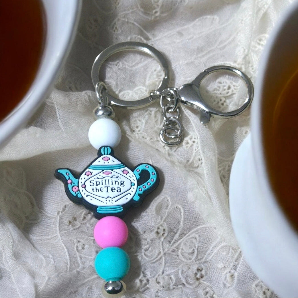 Keychain with "Spilling the Tea: teapot design and beads on a lace background. Inspired by Bridgerton.