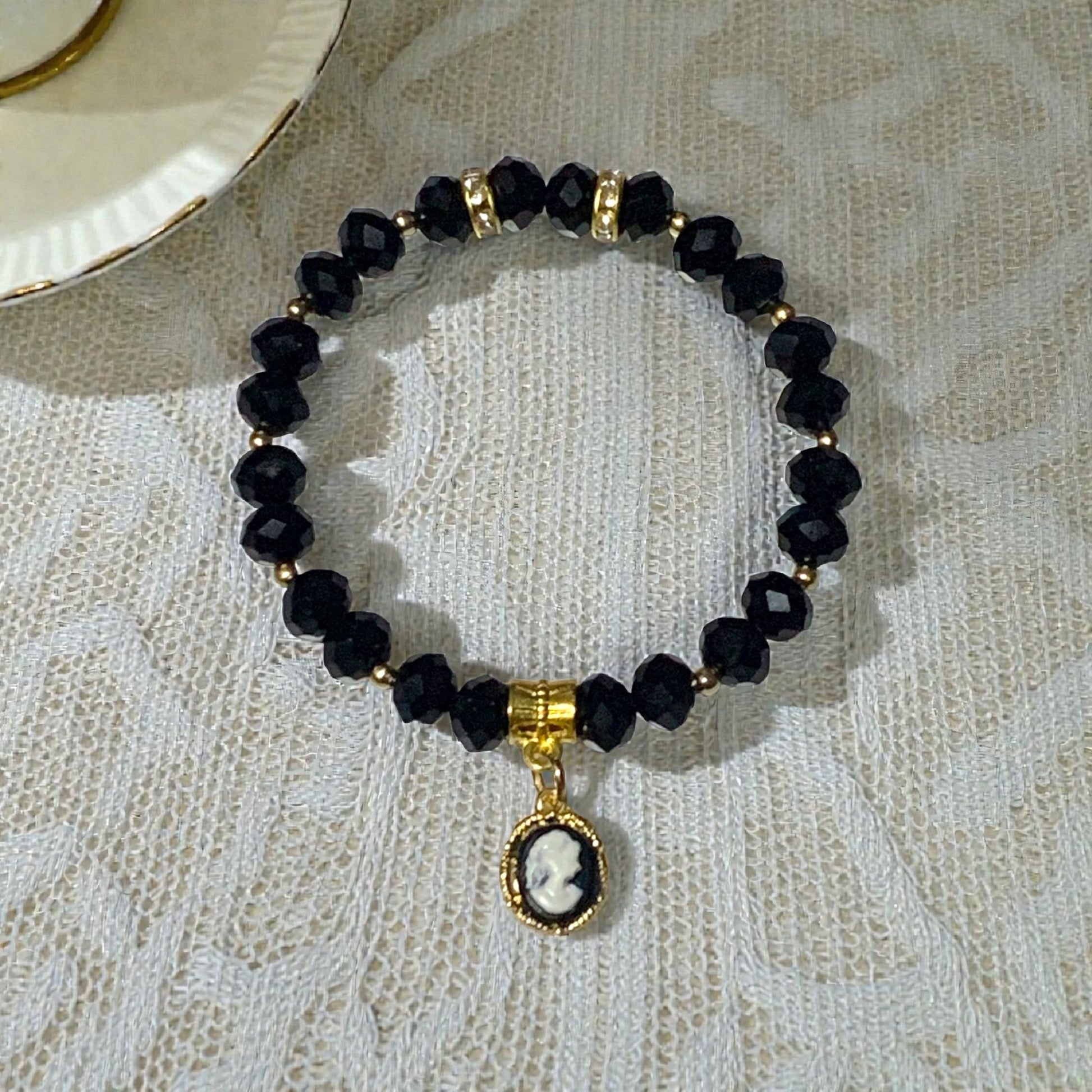 Regency inspired cameo stretch bracelet with crystal beads and gold charm styled on lace tablecloth beside vintage tea cup
