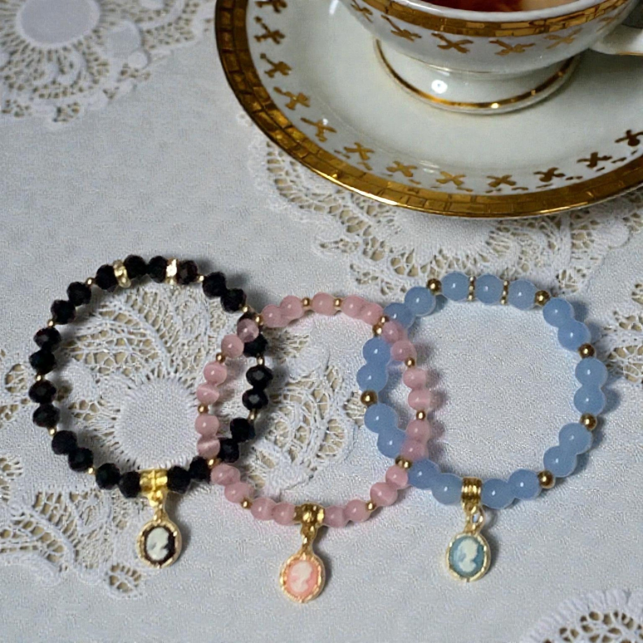 Regency inspired cameo stretch bracelets with crystal beads and gold charm styled on lace tablecloth beside vintage tea cup