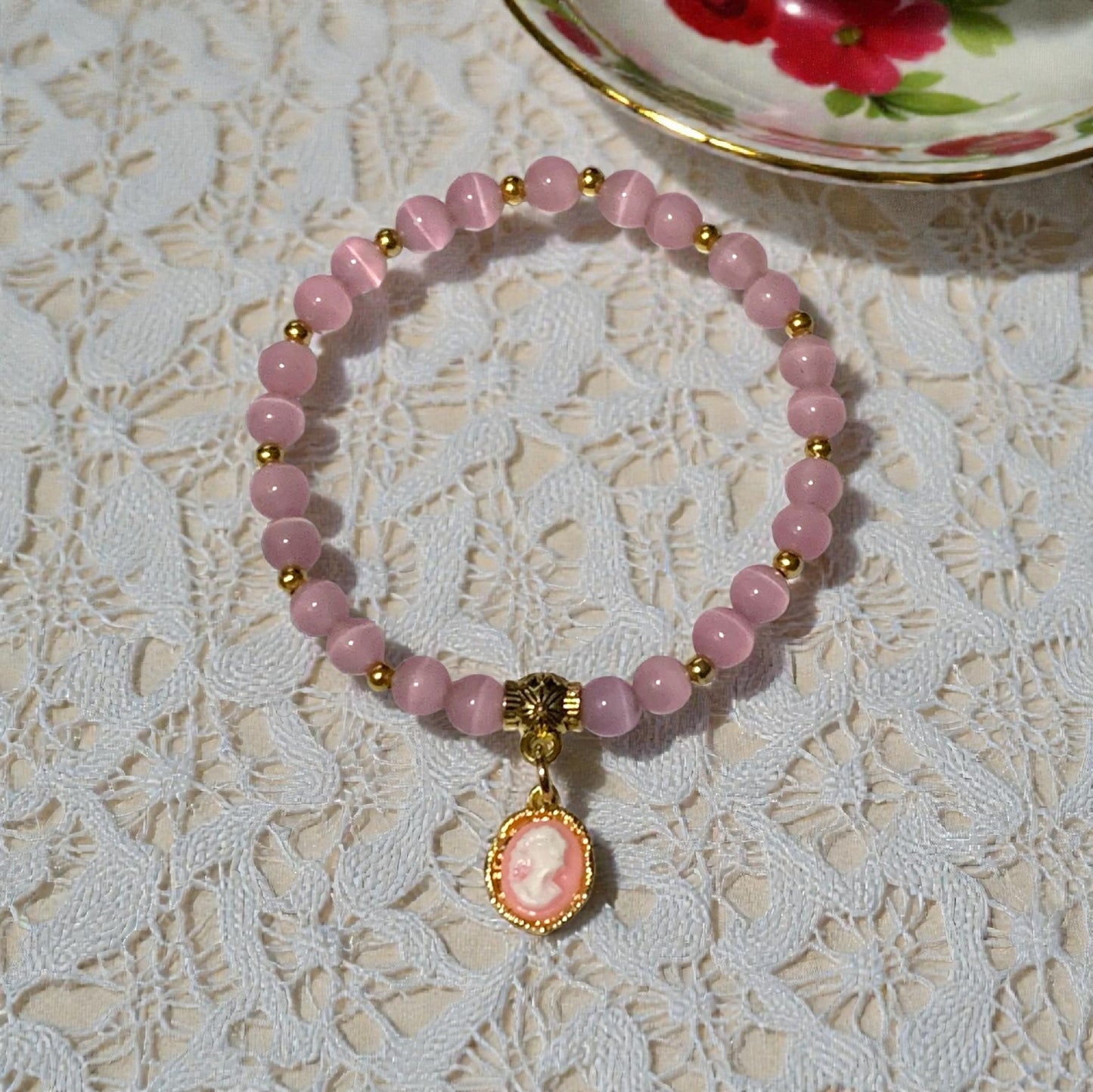 Regency inspired cameo stretch bracelet with crystal beads and gold charm styled on lace tablecloth beside vintage tea cup