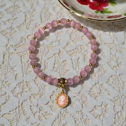 Regency inspired cameo stretch bracelet with crystal beads and gold charm styled on lace tablecloth beside vintage tea cup