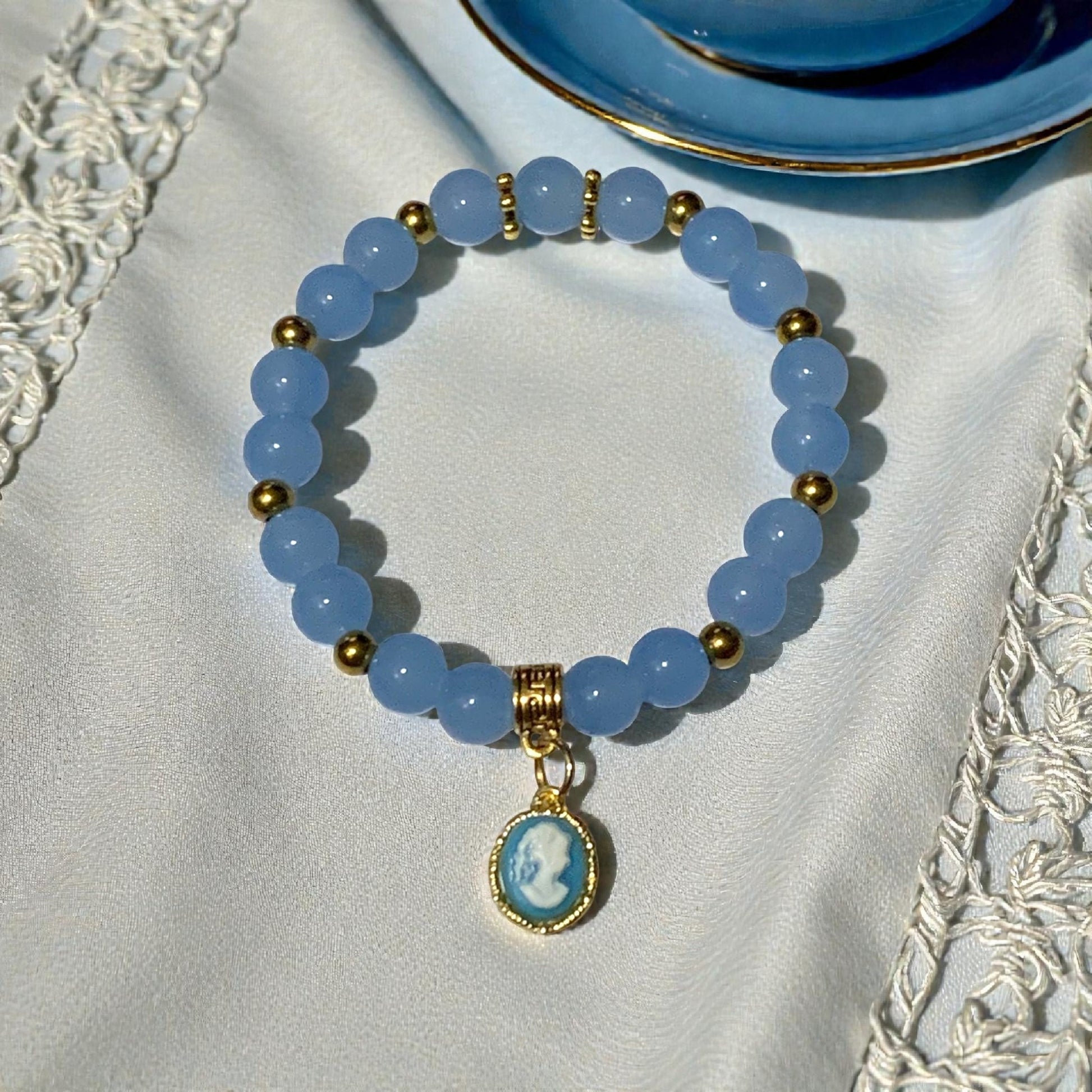 Bridgerton/Regency inspired cameo stretch bracelet with crystal beads and gold charm styled on lace tablecloth beside vintage tea cup.