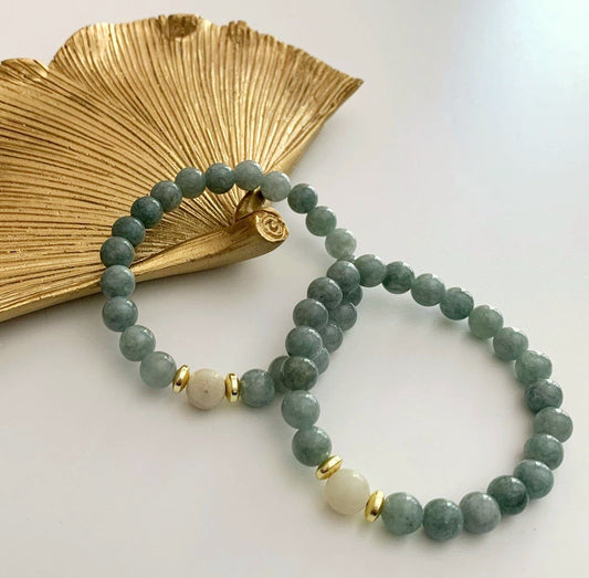 Burmese jade bracelet with a pale amazonite focal bead and gold-plated hematite accents displayed beside a gold decorative dish.