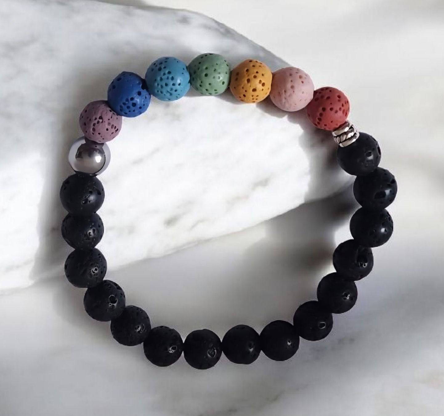 Chakra inspired lava stone bracelet with multicolor beads, black lava stones, stainless steel accent bead, and zinc alloy spacer on a white background.