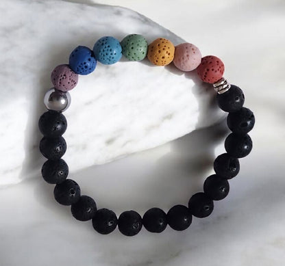 Chakra inspired lava stone bracelet with multicolor beads, black lava stones, stainless steel accent bead, and zinc alloy spacer on a white background.