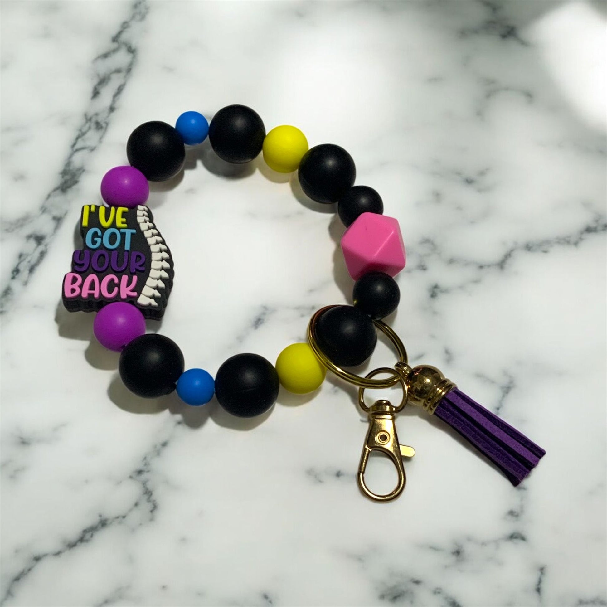 Colorful beaded bracelet with a keychain on a marble background. The focal bead is a human spine, and the text,  "I've Got Your Back."