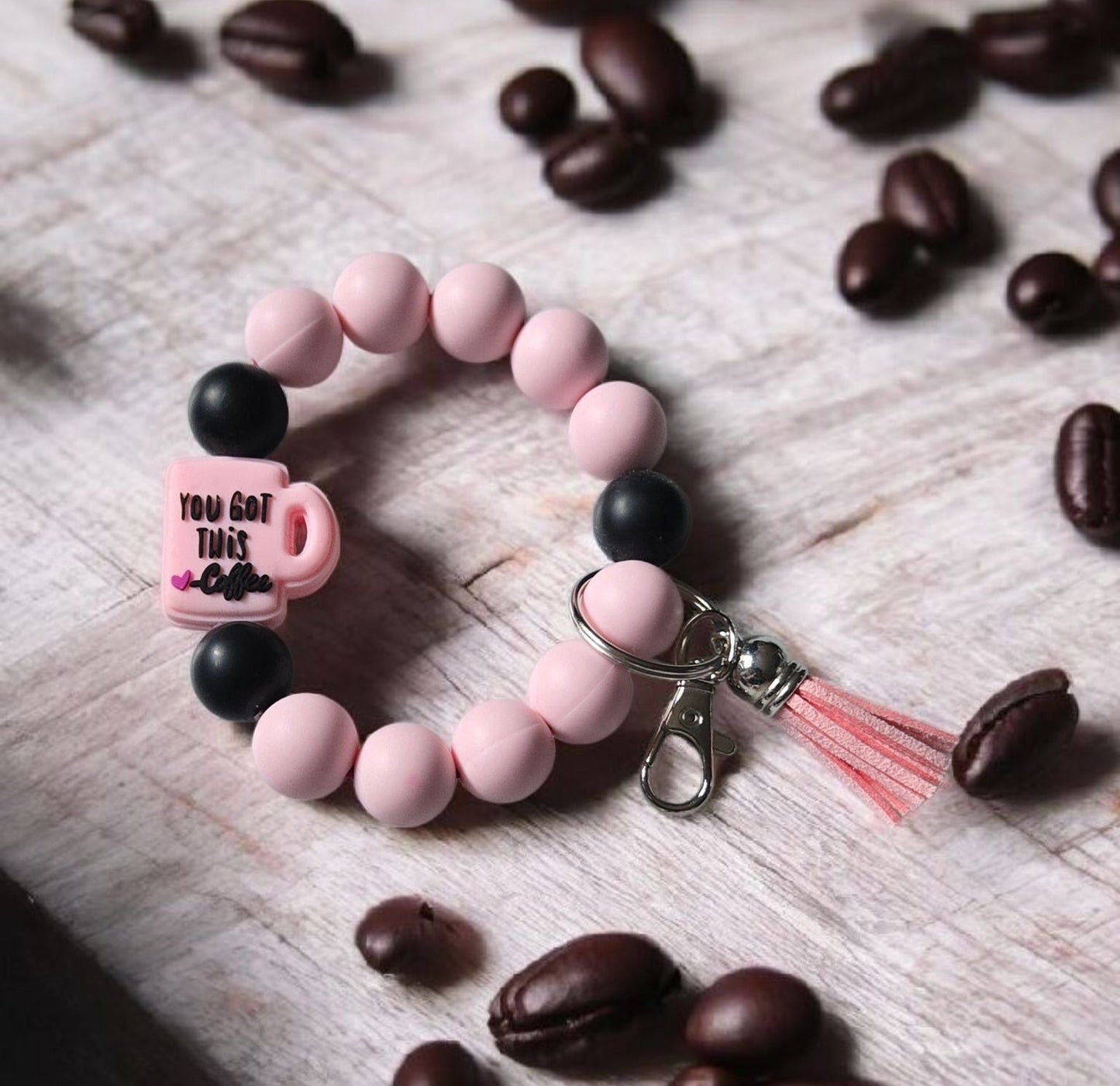 Pink beaded keychain bracelet with a focal bead saying,  "You Got This! - Coffee". The product is displayed on a wooden surface with coffee beans.