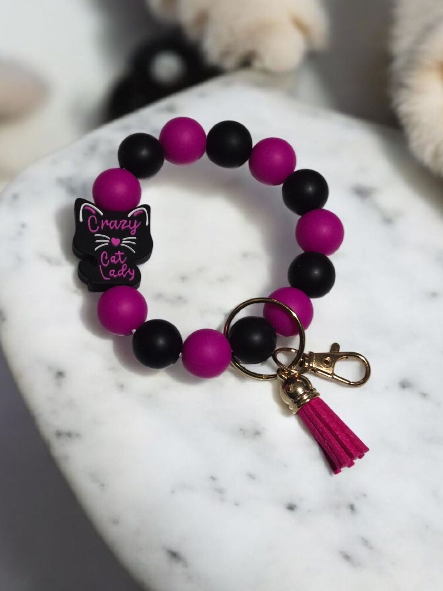 A keychain Bracelet with pink and black beads and a "Crazy Cat Lady" focal bead displayed on a marble surface.