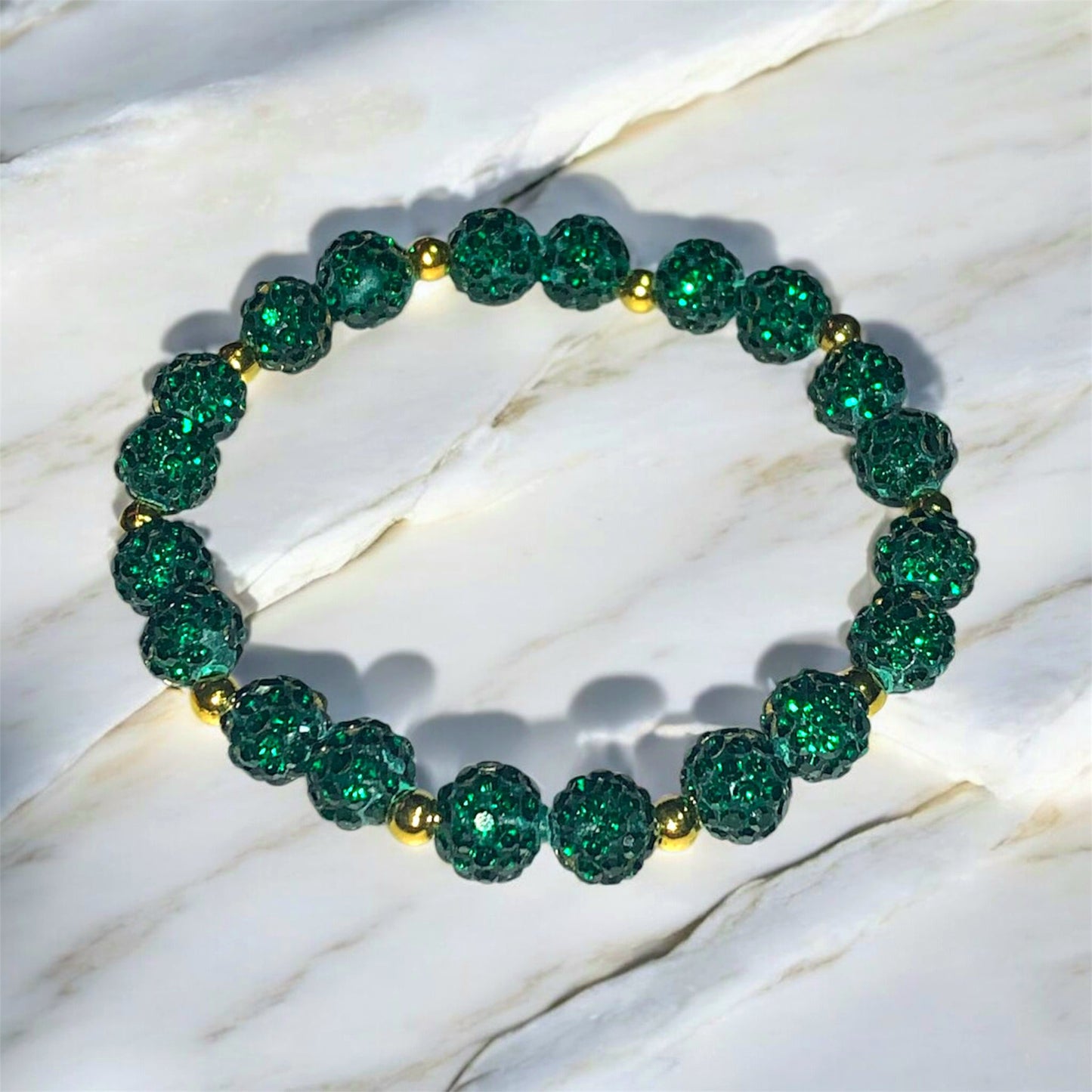A Bracelet made of dark green Shamballa beads and golden coloured stainless steel beads laying on a marble surface. Picture and bracelet by Divalicious Designs.