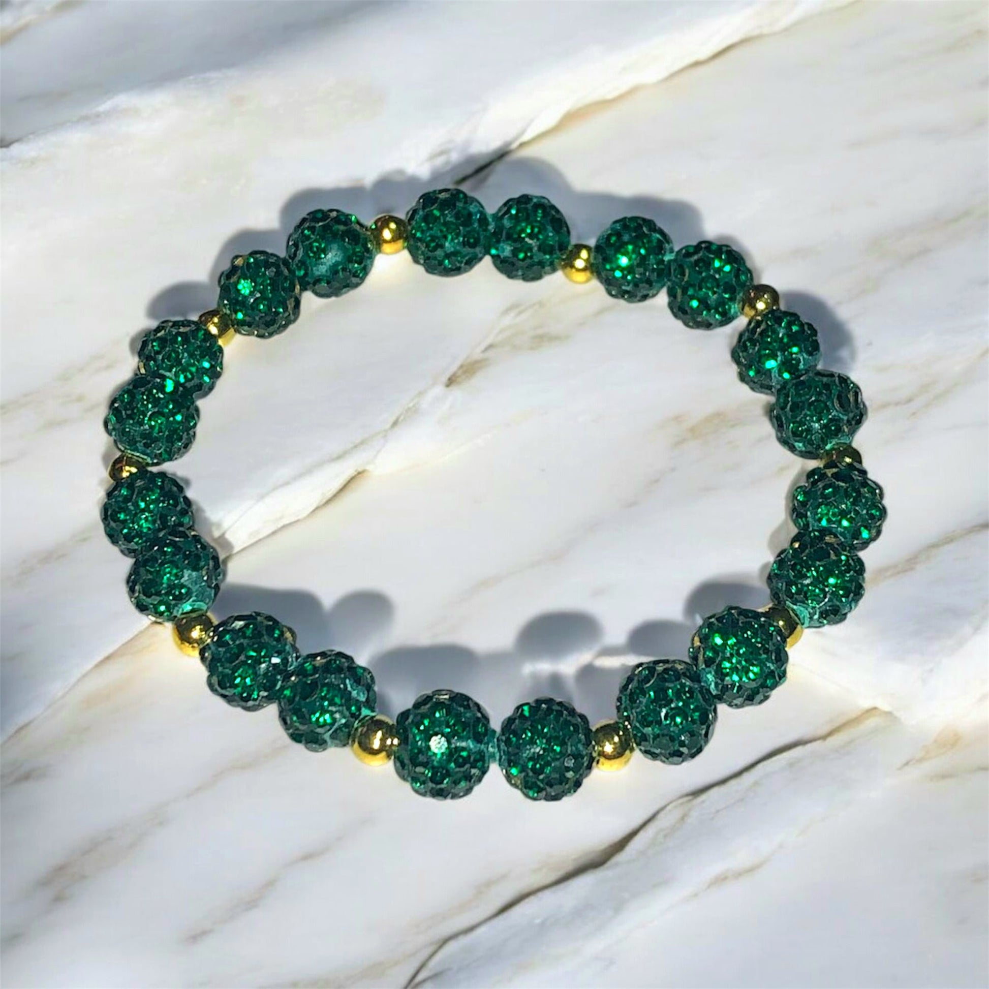 A Bracelet made of dark green Shamballa beads and golden coloured stainless steel beads laying on a marble surface. Picture and bracelet by Divalicious Designs.