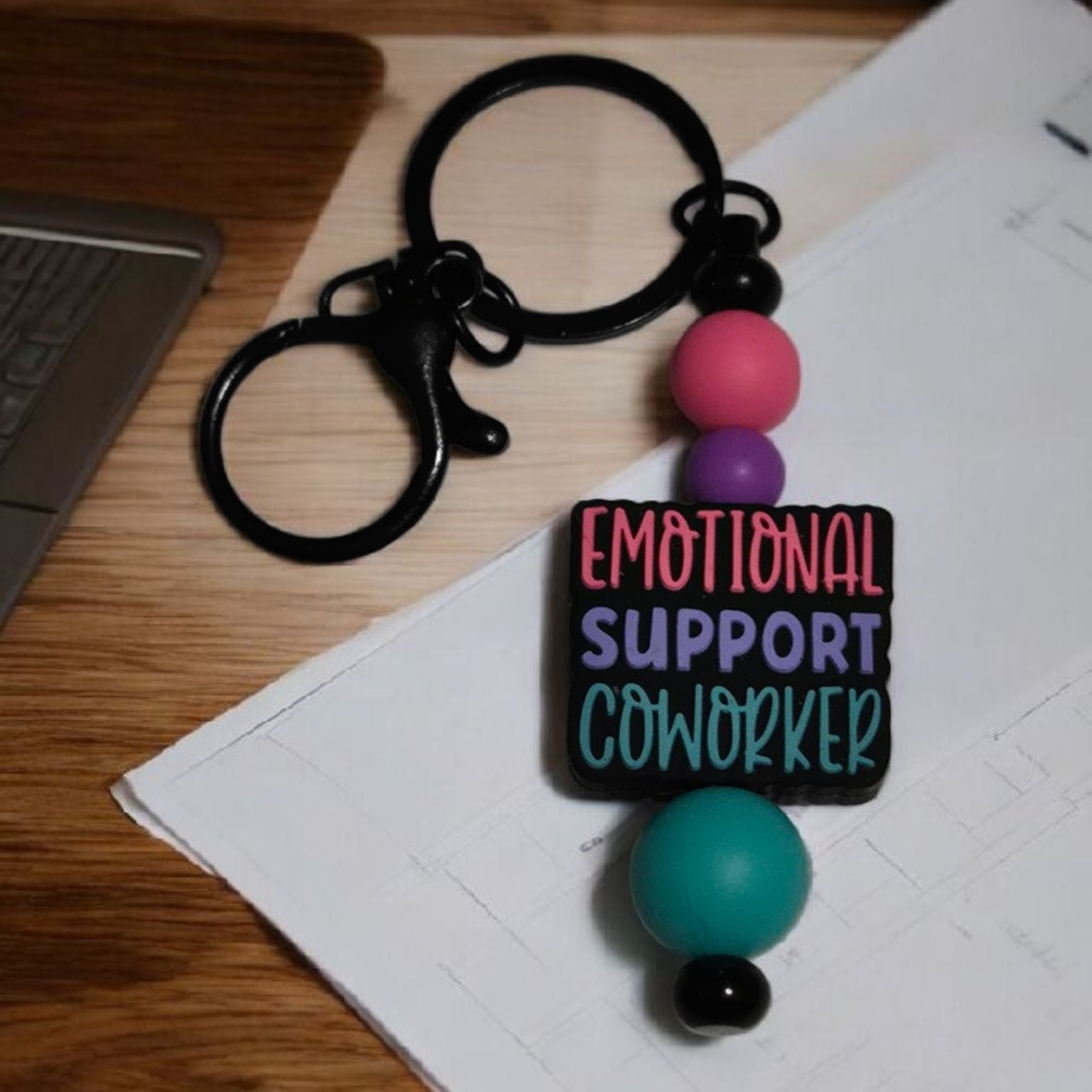 Keychain with colorful beads and 'Emotional Support Coworker' tag on a desk.