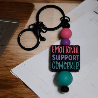 Keychain with colorful beads and 'Emotional Support Coworker' tag on a desk.