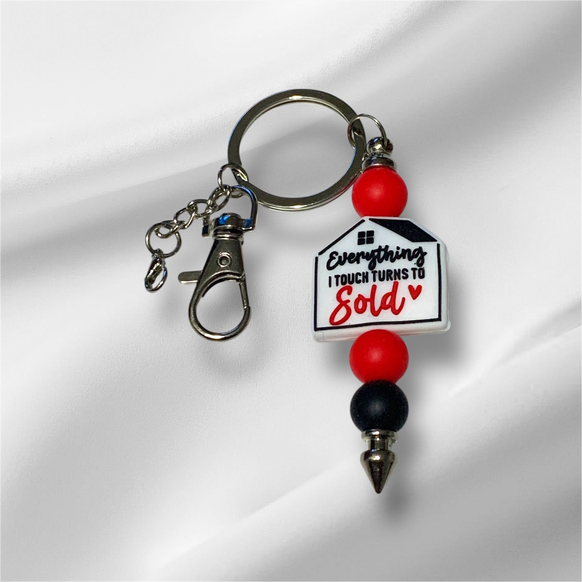 Keychain with house-shaped focal bead and red and black beads on a white background. The Focal bead states, "Everything I touch turns to sold."