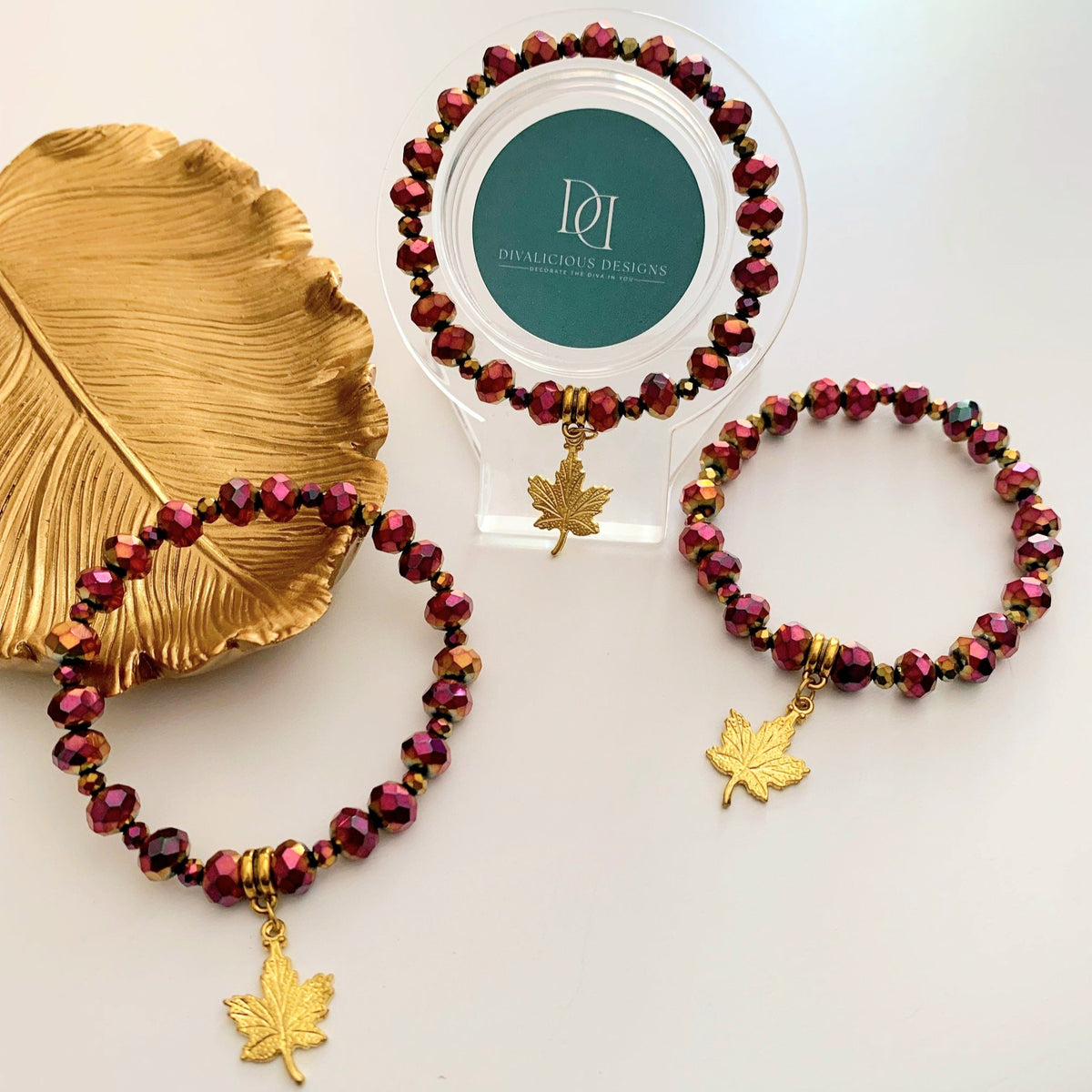 Red Chrome Crystal Bracelet with gold leaf charm on a white surface with a gold leaf and a branded card in the background. Made by Divalicious Designs.