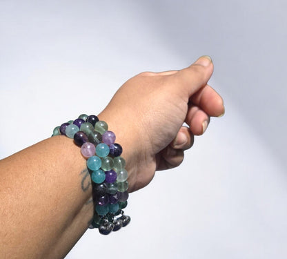 Handmade fluorite crystal stretch bracelet with green and purple beads and a silver heart charm displayed in natural light