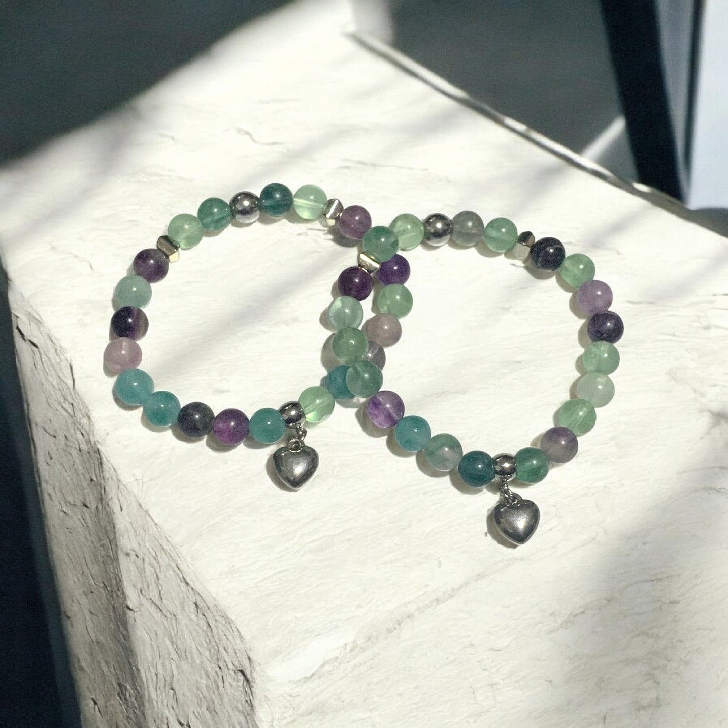 Handmade fluorite crystal stretch bracelet with green and purple beads and a silver heart charm displayed in natural light