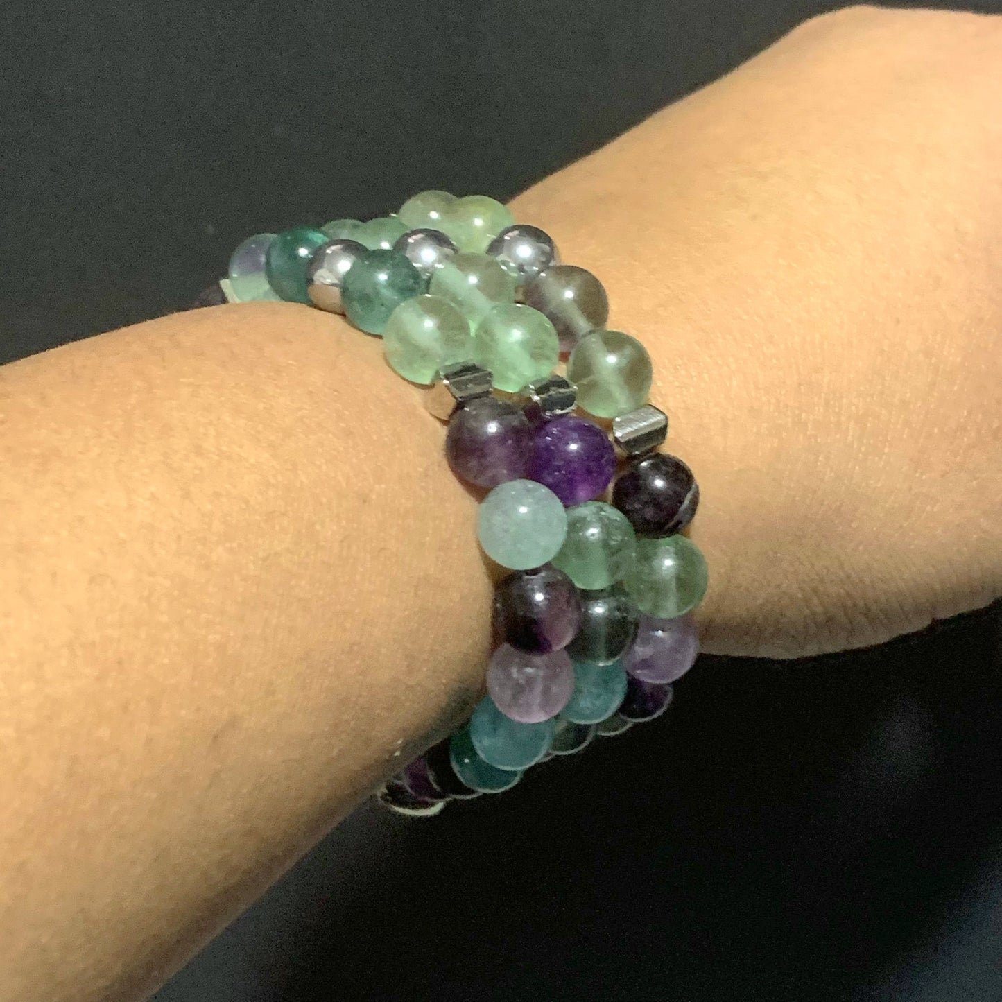 Handmade fluorite crystal stretch bracelet with green and purple beads and a silver heart charm displayed in natural light