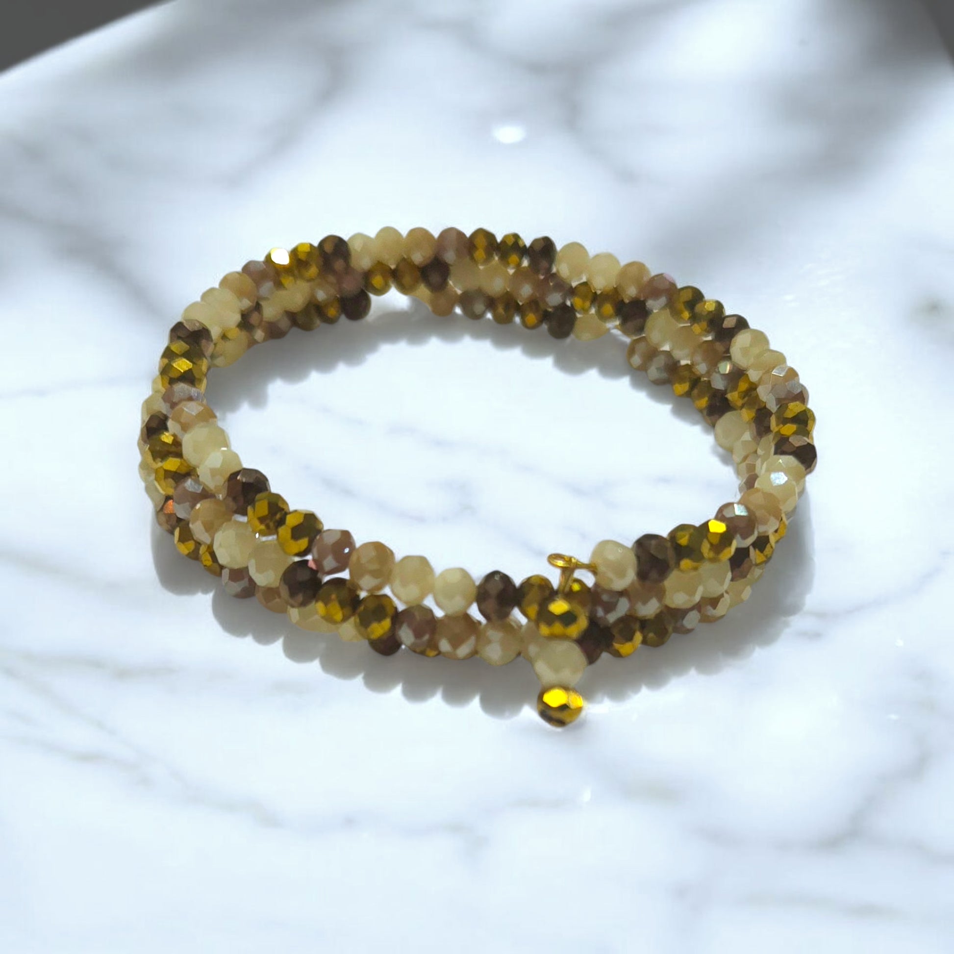 Gold and Neutral toned crystal wrap bracelet displayed on a white marble surface.