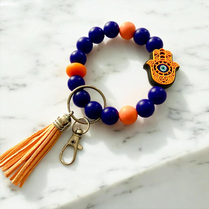 Beaded keychain with orange tassel and Hamsa hand charm on a marble. Orange and Purple