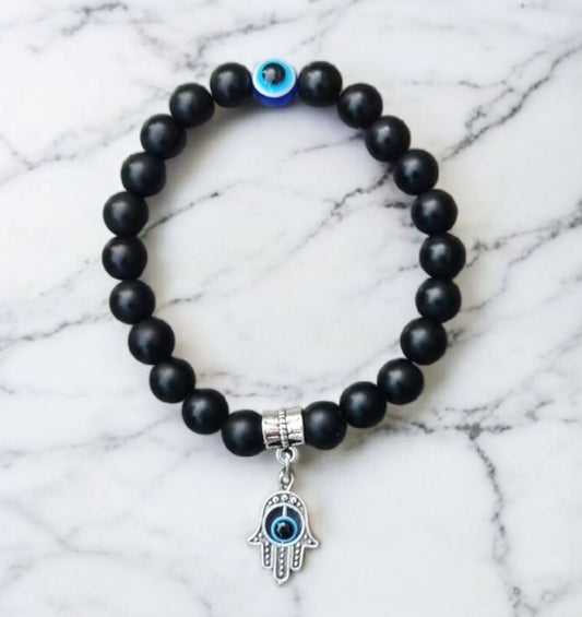 Black beaded bracelet with a silver Hamsa hand charm featuring an evil eye on a marble background. Photo and Bracelet by Divalicious Designs.