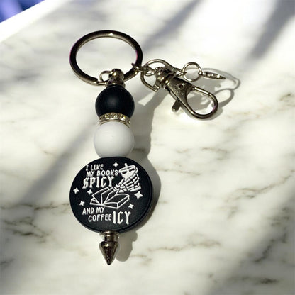Keychain with a black and white focal bead that says, "I Like My Books Spicy, and My Coffee Icy,"  on a marble surface