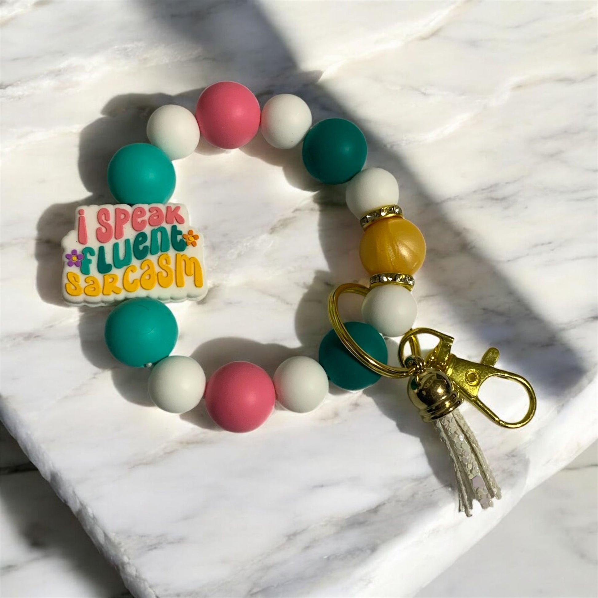 Colorful beaded keychain with 'I speak fluent sarcasm' tag on a marble surface