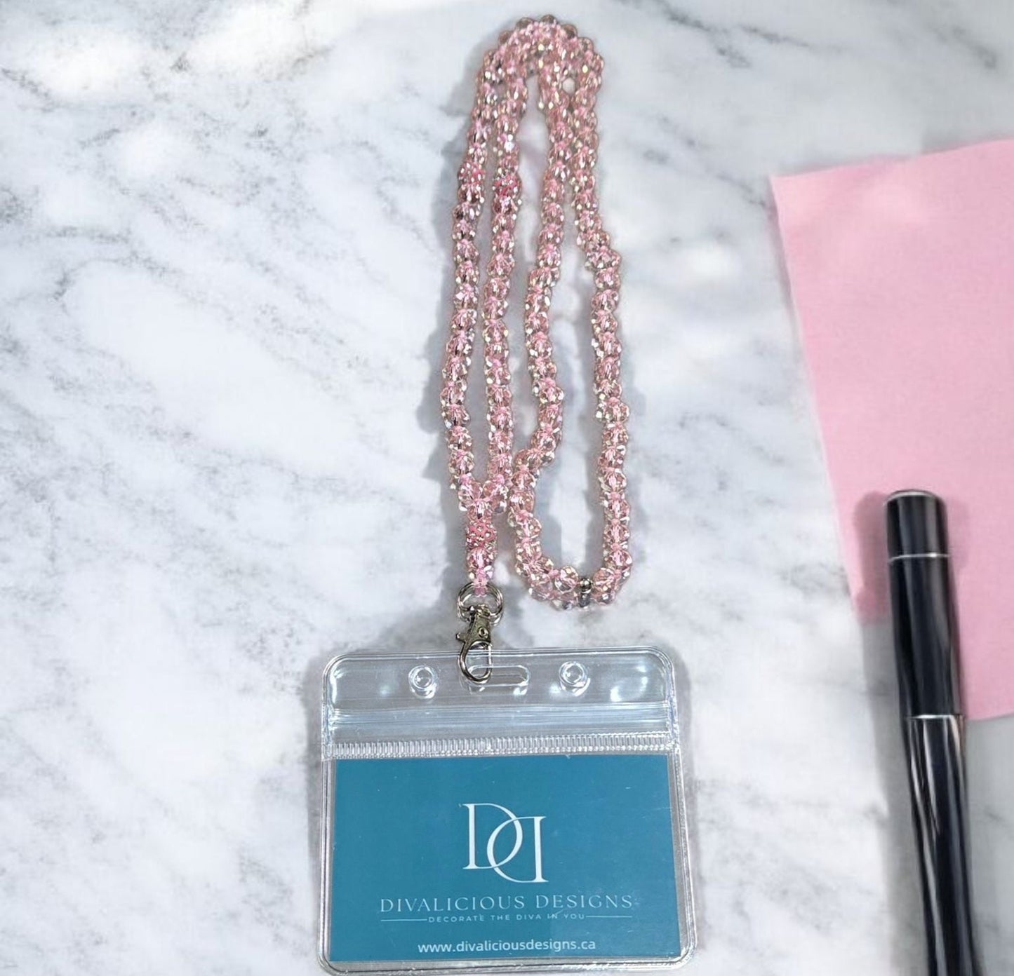 ID card holder with pink beaded chain on a marble surface with a pen and pink item.