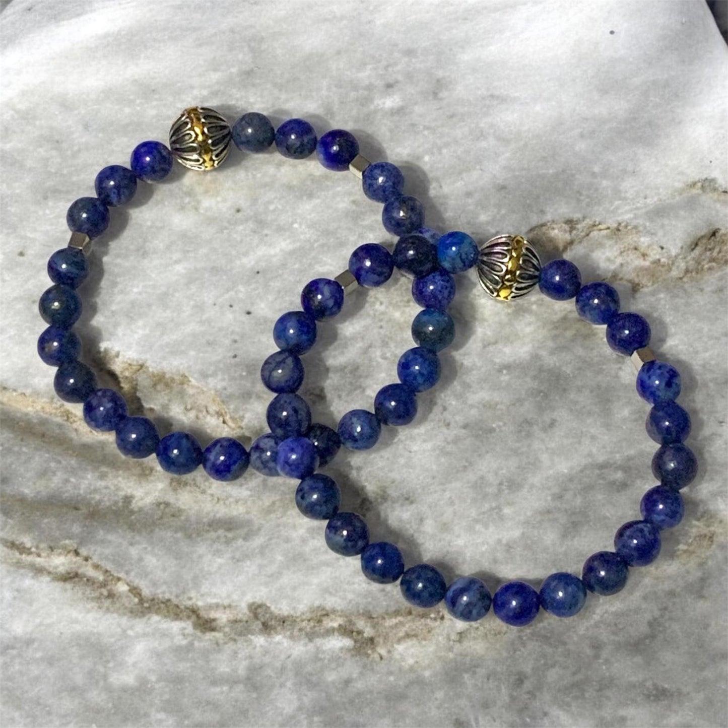 Handmade men’s Lapis Lazuli bracelet with stainless steel accents and silver gold Tibetan centerpiece bead on marble background by Divalicious Designs.