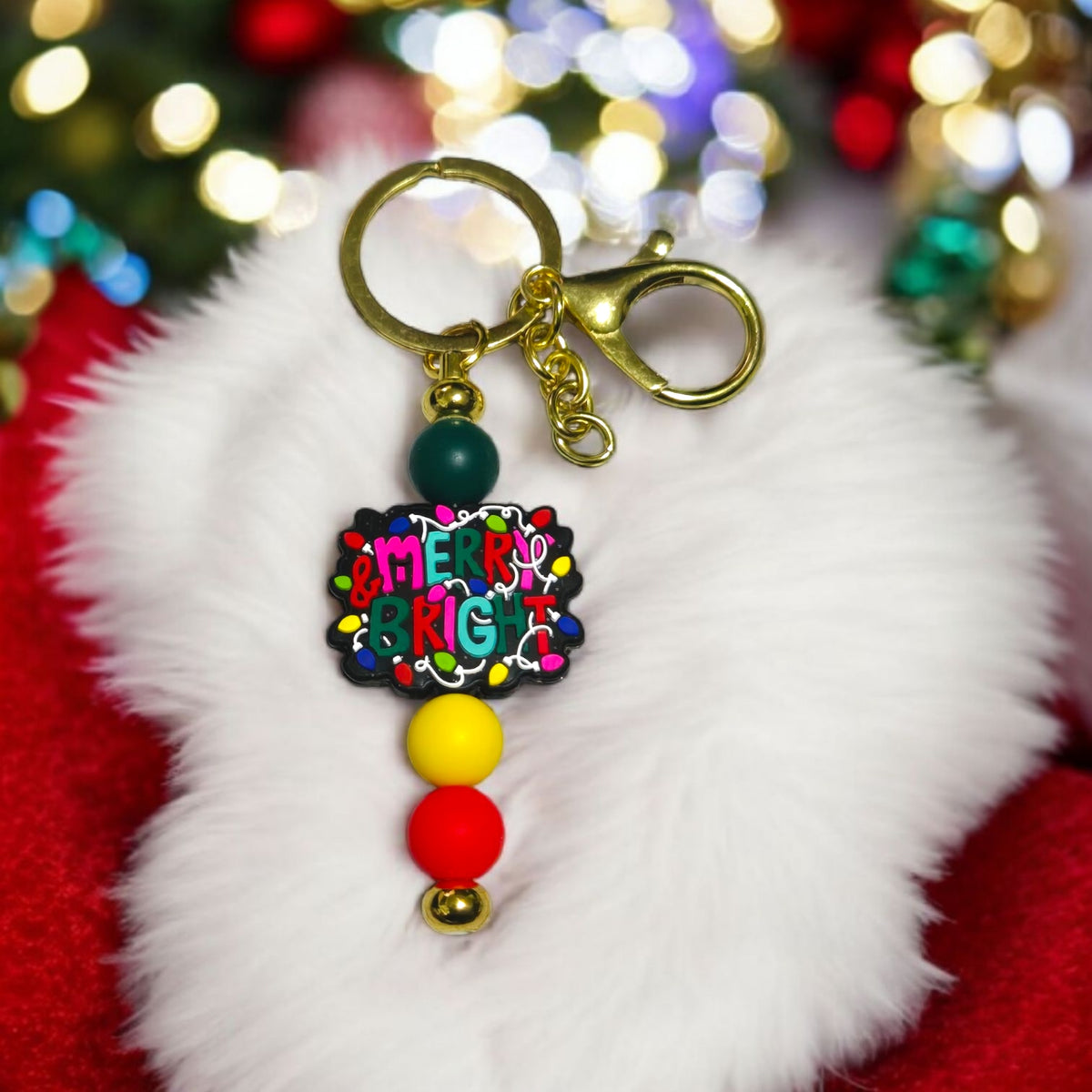 Colorful keychain with 'Merry Christmas' text on a fluffy white surface with blurred festive lights in the background.