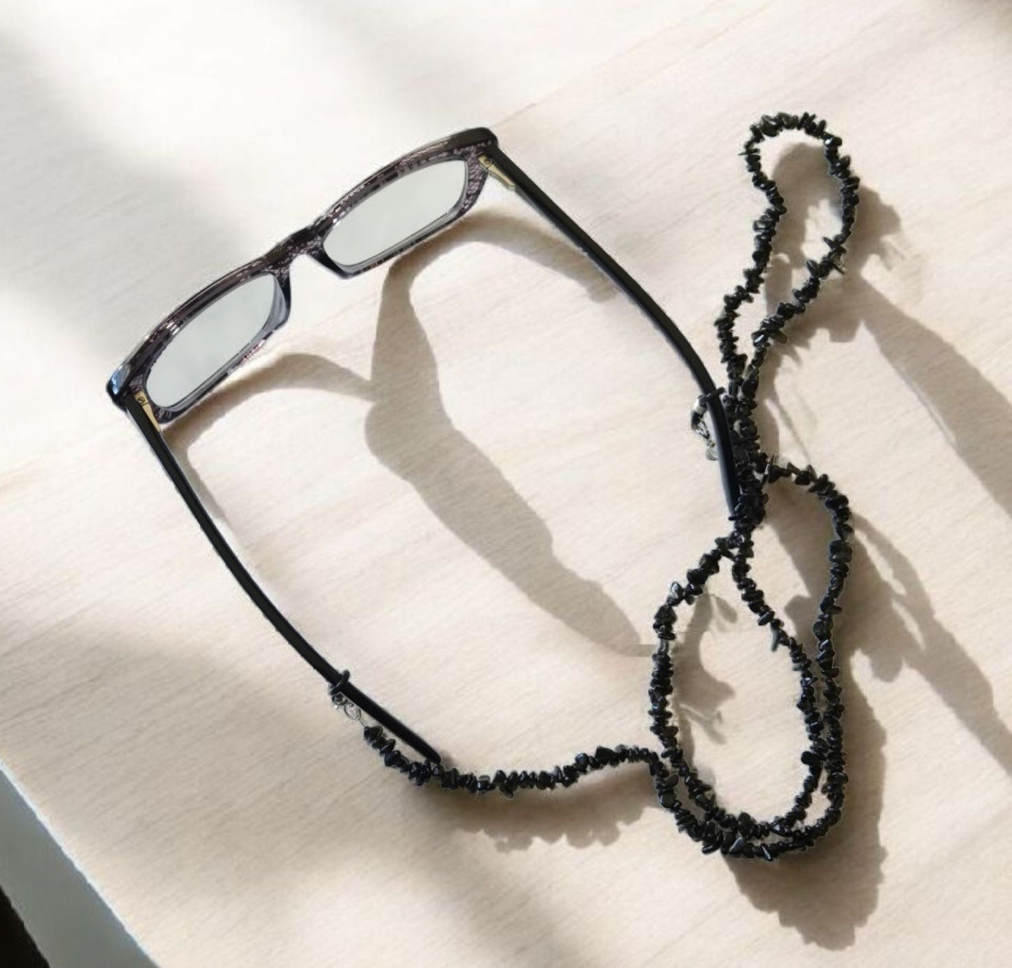 Eyeglasses with a black natural stone chip beaded strap on a light surface.