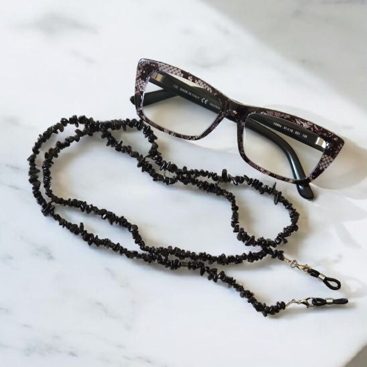 Black beaded eyeglass holder and glasses on a marble surface