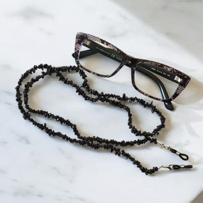 Black beaded eyeglass holder and glasses on a marble surface