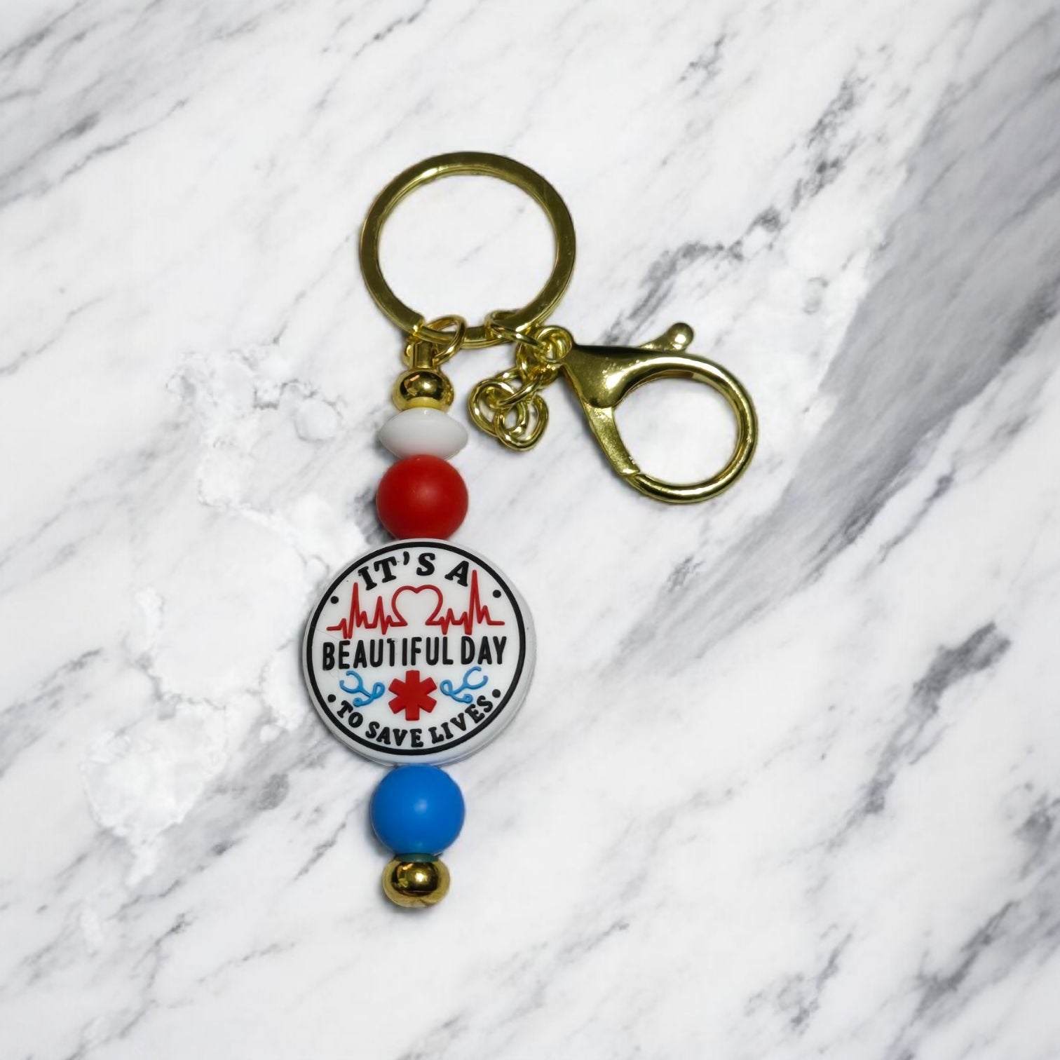 Keychain with colorful beads and a circular paramedic focal bead. Displayed on a light marble surface.
