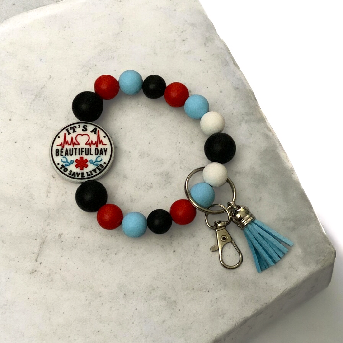 Colorful beaded keychain bracelet with a keychain and tassel on a marble surface.  The final bead is a parametic theme. 